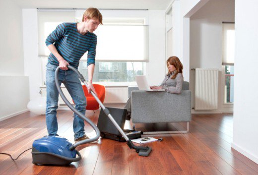 homem aspirando a sala enquanto mulher trabalha no sofá