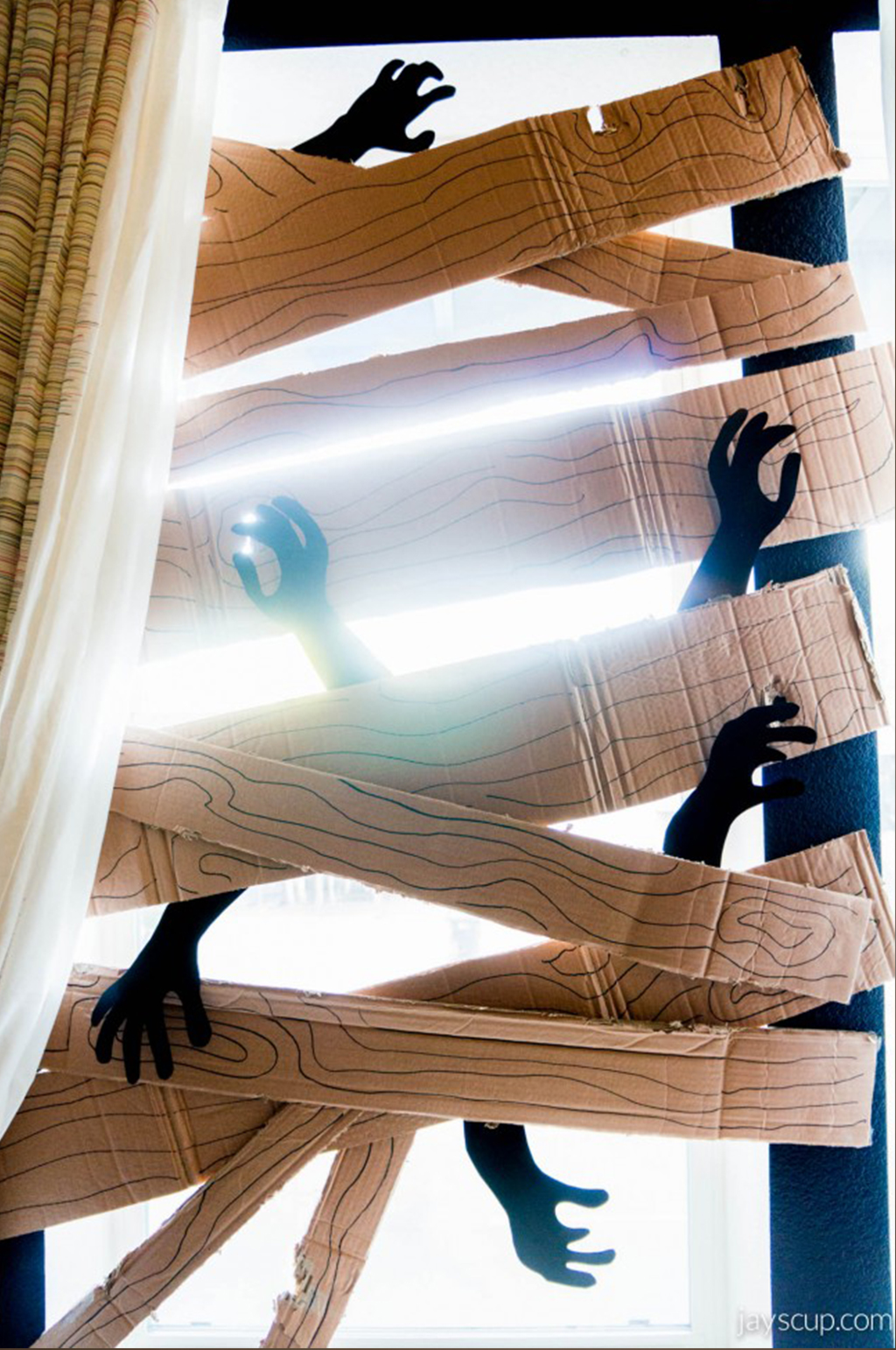 janela com várias tábuas feita de papelão aprisionando braços de zumbis 